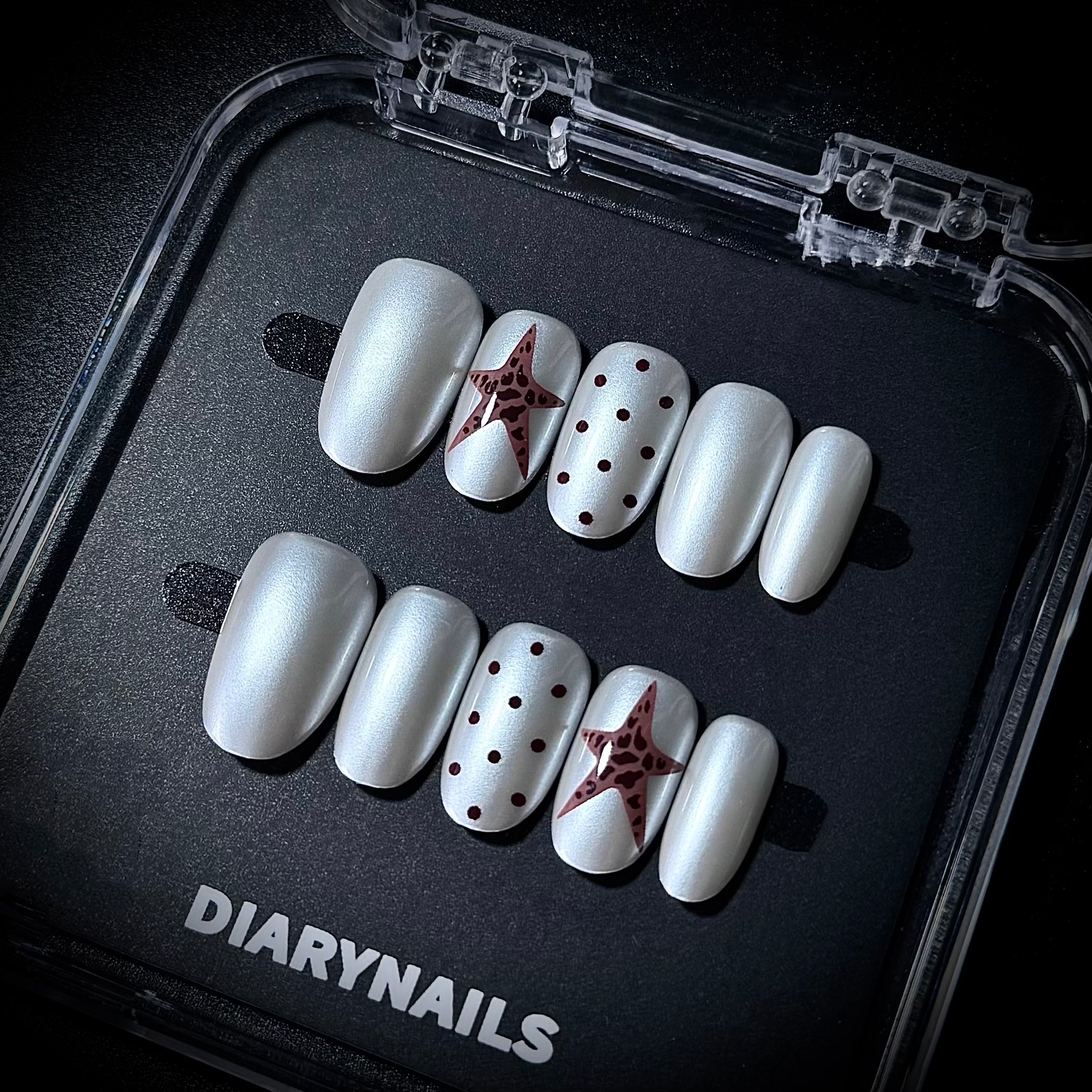 White press-on nails with star and dot designs in a clear case, branded 'DIARYNAILS'.